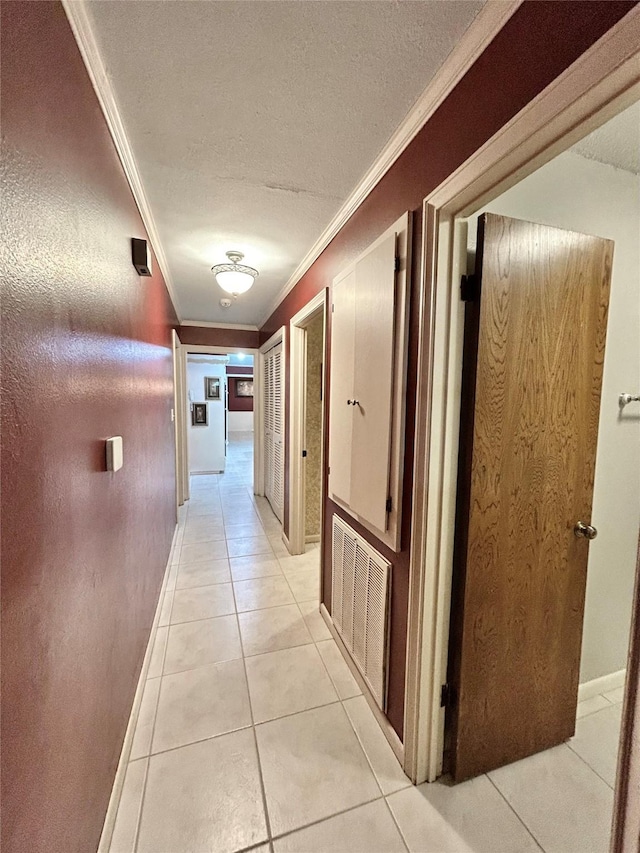 hallway featuring light tile patterned floors, a textured ceiling, visible vents, baseboards, and ornamental molding