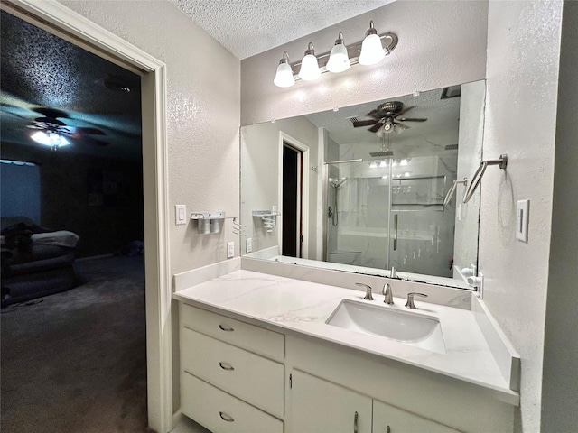 bathroom with a textured wall, ceiling fan, a textured ceiling, a shower stall, and vanity