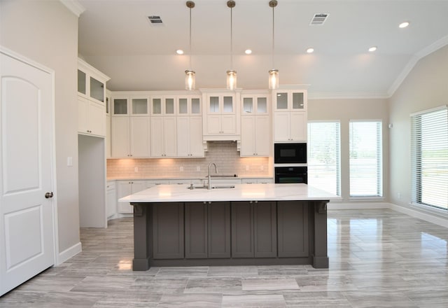 kitchen with hanging light fixtures, vaulted ceiling, a kitchen island with sink, white cabinets, and black appliances