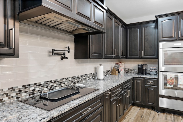 kitchen featuring extractor fan, light stone counters, stainless steel double oven, black electric stovetop, and backsplash