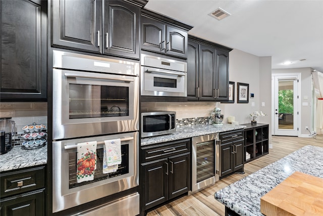 kitchen with light hardwood / wood-style flooring, stainless steel appliances, wine cooler, light stone counters, and decorative backsplash