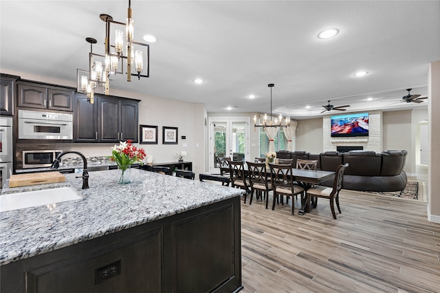 kitchen with pendant lighting, sink, a large fireplace, light hardwood / wood-style floors, and stainless steel appliances