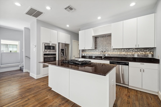 kitchen with a center island, dark hardwood / wood-style flooring, stainless steel appliances, white cabinets, and backsplash