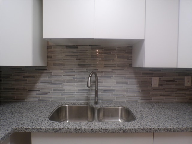 room details featuring sink, light stone countertops, decorative backsplash, and white cabinetry