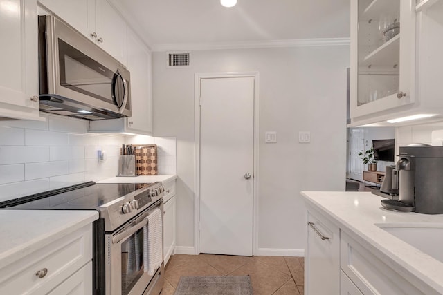 kitchen with white cabinetry, crown molding, decorative backsplash, light tile patterned floors, and appliances with stainless steel finishes