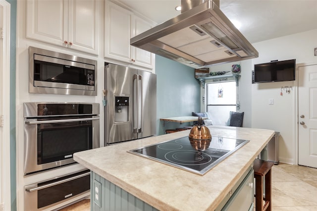 kitchen with a center island, white cabinets, light tile patterned floors, island range hood, and stainless steel appliances