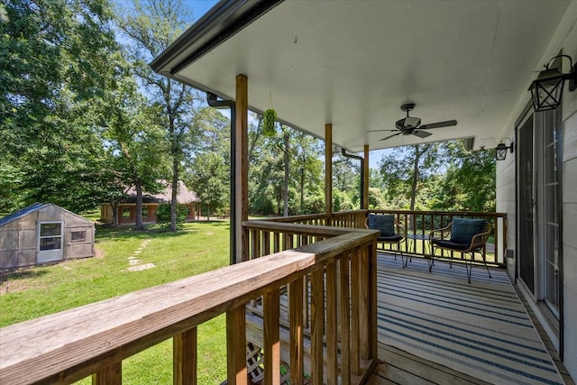 wooden terrace featuring a shed, ceiling fan, and a lawn