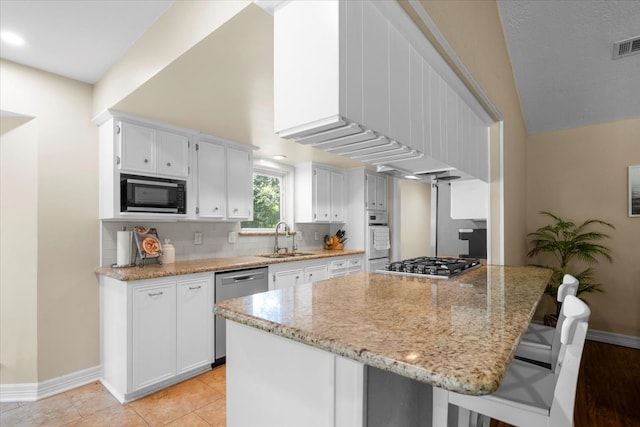 kitchen with light stone countertops, appliances with stainless steel finishes, sink, white cabinets, and a breakfast bar