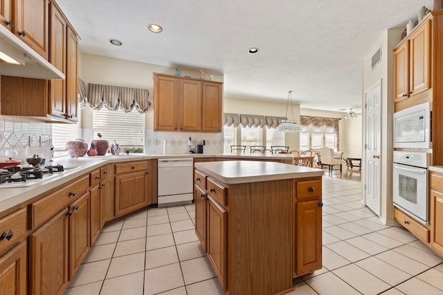 kitchen featuring decorative light fixtures, white appliances, a center island, light tile patterned floors, and backsplash