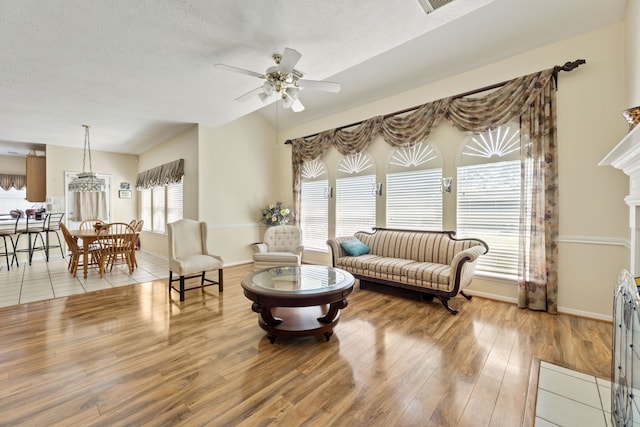 living room with hardwood / wood-style flooring, ceiling fan, vaulted ceiling, and a textured ceiling