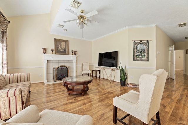 living room with ceiling fan, a tile fireplace, crown molding, and light wood-type flooring