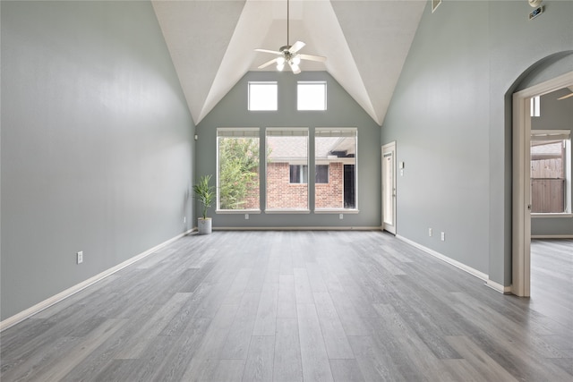 unfurnished living room with ceiling fan, a towering ceiling, and light wood-type flooring