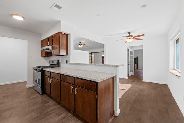 kitchen with light stone counters, stainless steel gas range, dark wood-type flooring, kitchen peninsula, and decorative backsplash