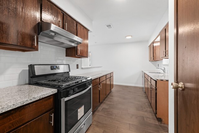 kitchen featuring sink, stainless steel gas range, tasteful backsplash, dark hardwood / wood-style flooring, and extractor fan