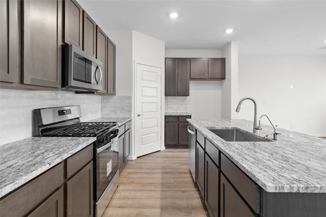 kitchen with stainless steel appliances, sink, an island with sink, light hardwood / wood-style flooring, and decorative backsplash