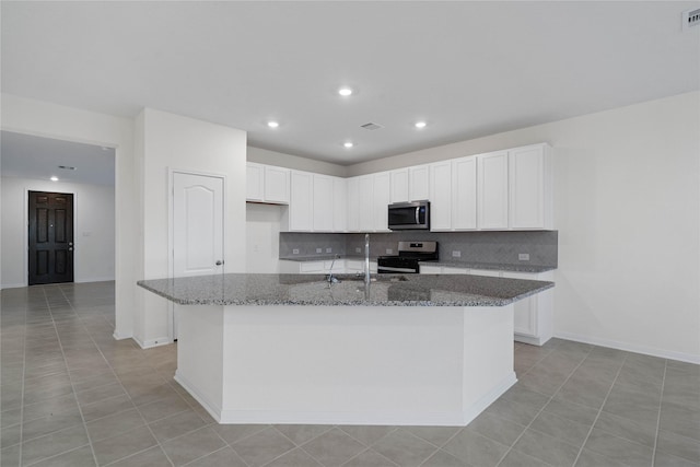 kitchen featuring dark stone countertops, white cabinetry, an island with sink, and appliances with stainless steel finishes