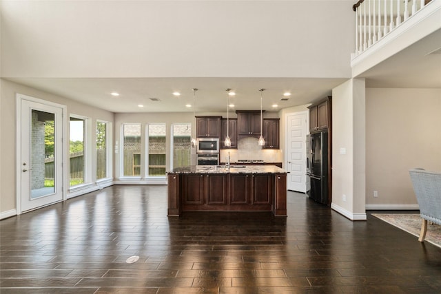 kitchen featuring pendant lighting, dark wood-type flooring, a center island with sink, decorative backsplash, and appliances with stainless steel finishes