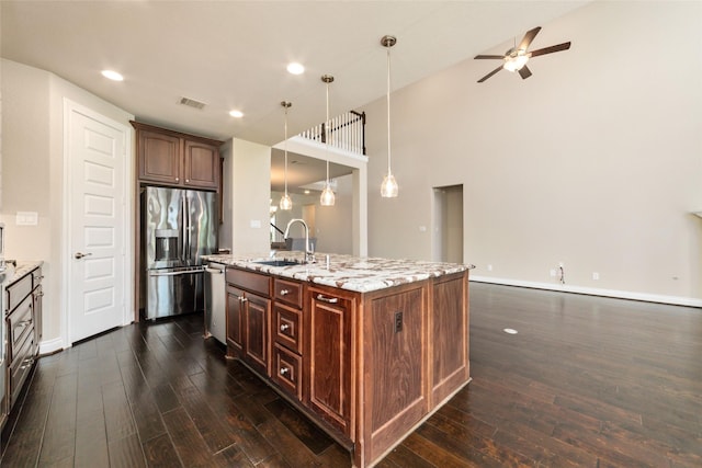 kitchen with a kitchen island with sink, sink, appliances with stainless steel finishes, decorative light fixtures, and dark hardwood / wood-style flooring