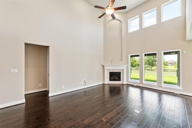 unfurnished living room with a high ceiling, dark hardwood / wood-style flooring, ceiling fan, and a tiled fireplace