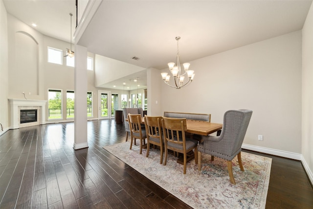 dining area featuring dark hardwood / wood-style flooring, a premium fireplace, a high ceiling, and an inviting chandelier