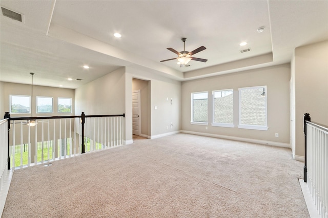 spare room featuring a raised ceiling, ceiling fan, and light colored carpet