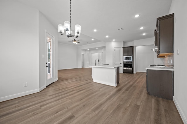 kitchen featuring stainless steel appliances, an island with sink, dark hardwood / wood-style floors, dark brown cabinets, and wall chimney range hood