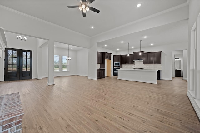 unfurnished living room featuring sink, french doors, light hardwood / wood-style floors, ceiling fan with notable chandelier, and crown molding