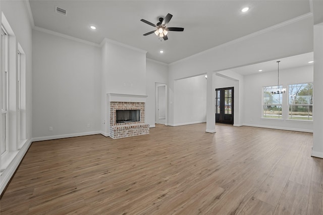 unfurnished living room featuring ceiling fan with notable chandelier, a brick fireplace, light hardwood / wood-style floors, and crown molding