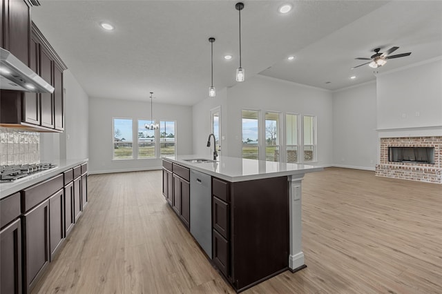 kitchen featuring sink, ceiling fan with notable chandelier, a brick fireplace, a kitchen island with sink, and appliances with stainless steel finishes