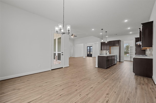 kitchen featuring tasteful backsplash, pendant lighting, light hardwood / wood-style flooring, ceiling fan with notable chandelier, and a kitchen island with sink