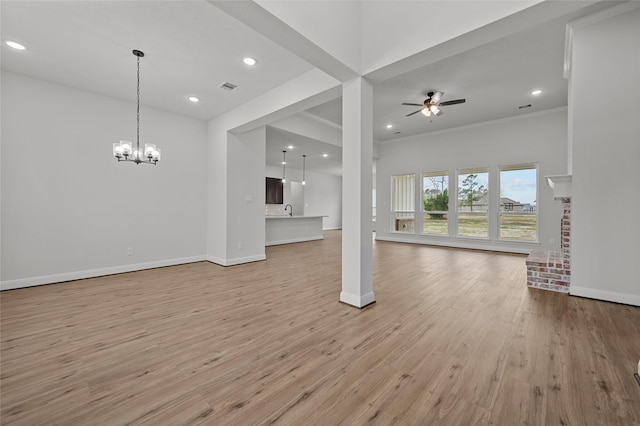 unfurnished living room with ceiling fan with notable chandelier, a fireplace, light wood-type flooring, and ornamental molding