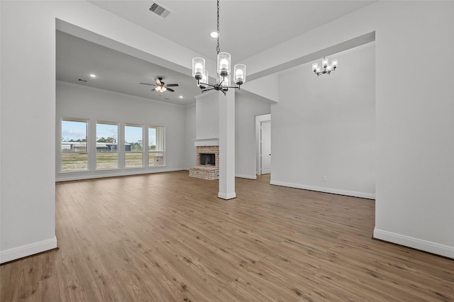 unfurnished living room with ceiling fan with notable chandelier, a fireplace, ornamental molding, and hardwood / wood-style flooring