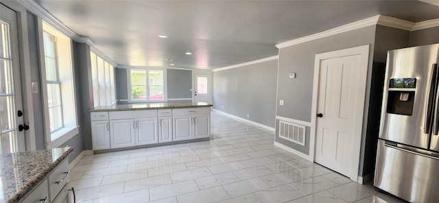 kitchen with stainless steel fridge, light stone counters, white cabinetry, and ornamental molding