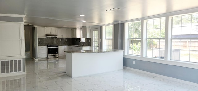 kitchen with kitchen peninsula, dark stone countertops, stainless steel range, tasteful backsplash, and white cabinetry