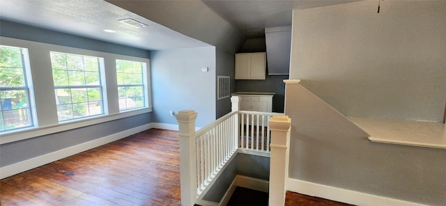 staircase featuring a textured ceiling, wood-type flooring, and vaulted ceiling