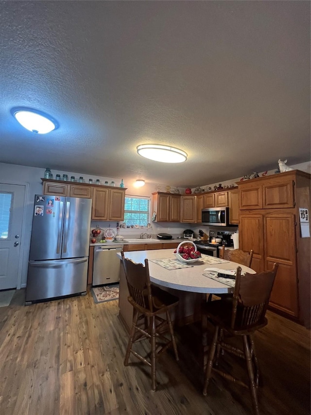 kitchen featuring a kitchen breakfast bar, stainless steel appliances, a textured ceiling, and light wood-type flooring