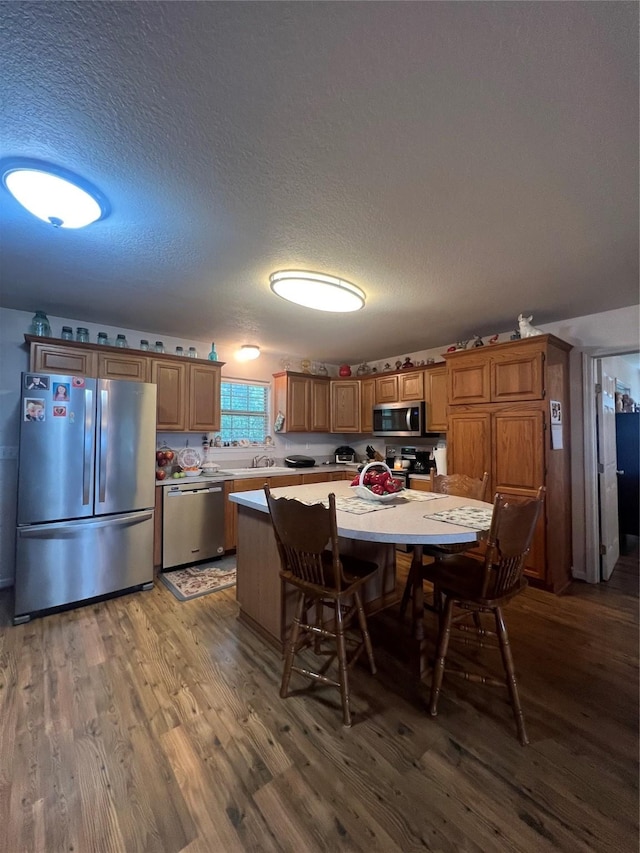 kitchen with a textured ceiling, a kitchen island, stainless steel appliances, and hardwood / wood-style floors