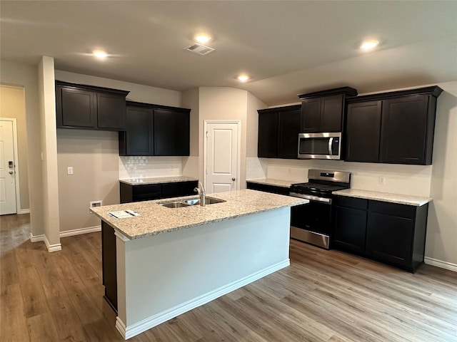 kitchen with light stone counters, a kitchen island with sink, sink, light hardwood / wood-style floors, and stainless steel appliances