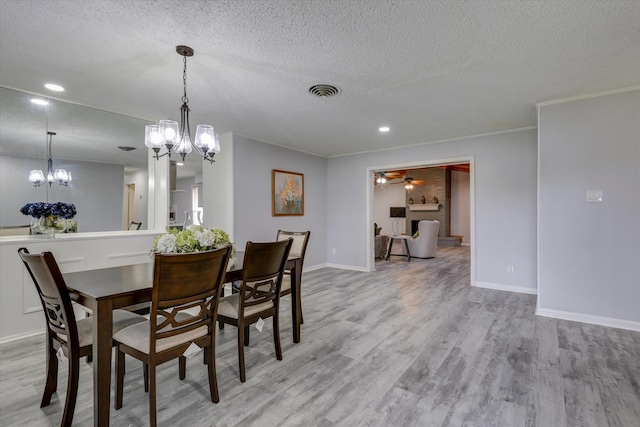 dining space with crown molding, light wood-type flooring, ceiling fan with notable chandelier, and a textured ceiling