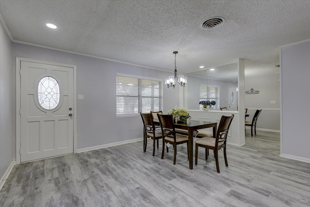 dining area with a textured ceiling, light hardwood / wood-style flooring, ornamental molding, and a notable chandelier