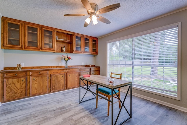 dining space with ceiling fan, a textured ceiling, ornamental molding, and light hardwood / wood-style floors