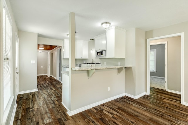 kitchen with a breakfast bar area, dark hardwood / wood-style floors, light stone counters, white cabinets, and built in microwave