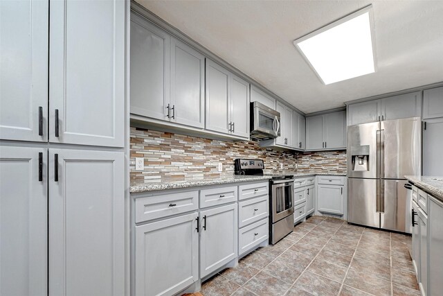 kitchen with light stone counters, light tile floors, backsplash, and appliances with stainless steel finishes