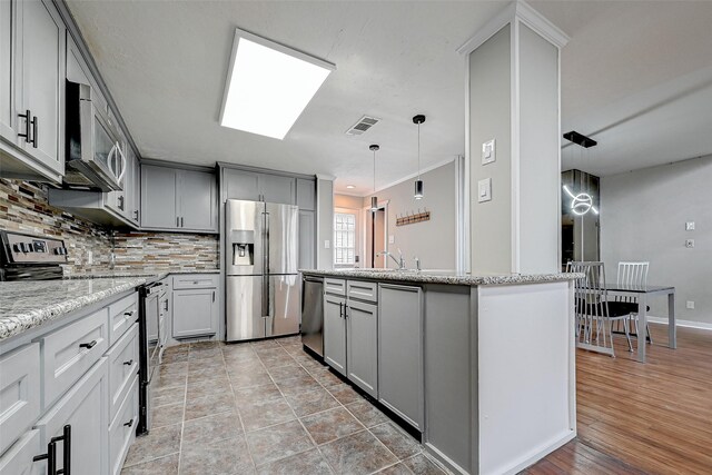 kitchen with stainless steel appliances, hanging light fixtures, tasteful backsplash, and light tile floors