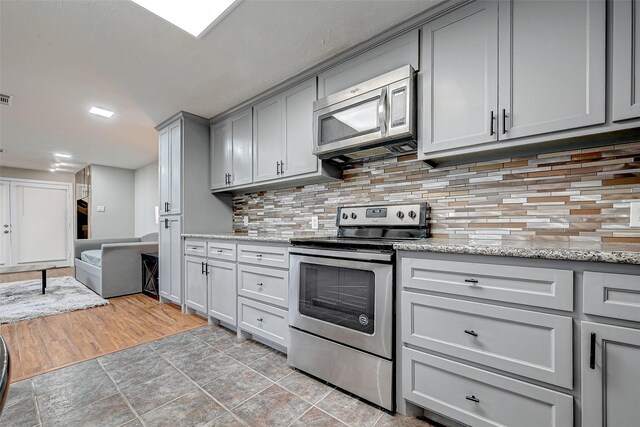 kitchen featuring appliances with stainless steel finishes, tasteful backsplash, light stone counters, and light hardwood / wood-style flooring