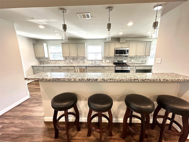 kitchen featuring sink, light stone counters, hanging light fixtures, a breakfast bar, and appliances with stainless steel finishes