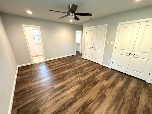 unfurnished bedroom featuring ensuite bathroom, multiple closets, ceiling fan, and dark wood-type flooring