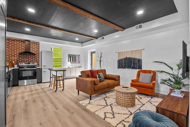 living room featuring beam ceiling, brick wall, a wood stove, and light hardwood / wood-style flooring