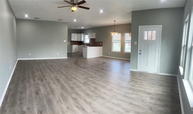 unfurnished living room with ceiling fan with notable chandelier and light hardwood / wood-style floors