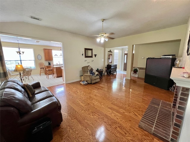 living room featuring a textured ceiling, vaulted ceiling, light hardwood / wood-style flooring, and ceiling fan